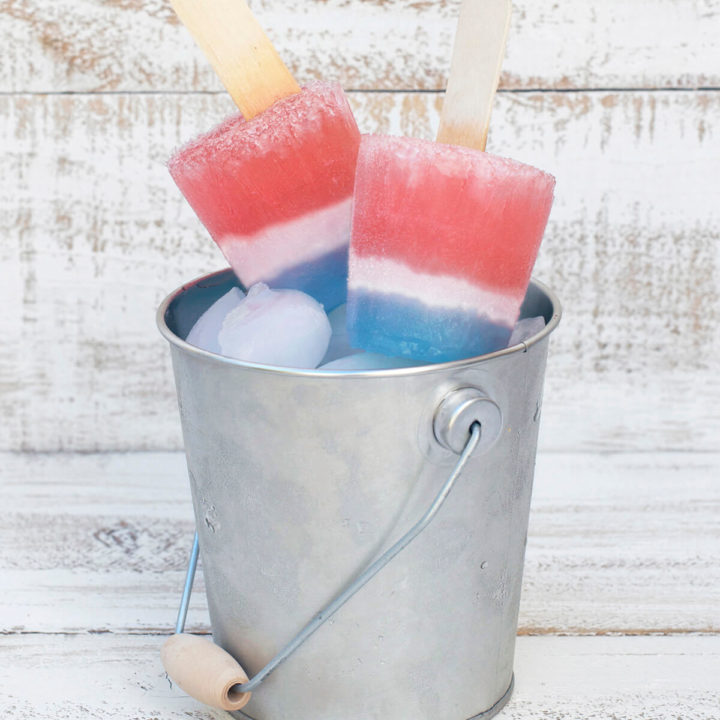 Two red, white and blue popsicles sitting in a small bucket of ice