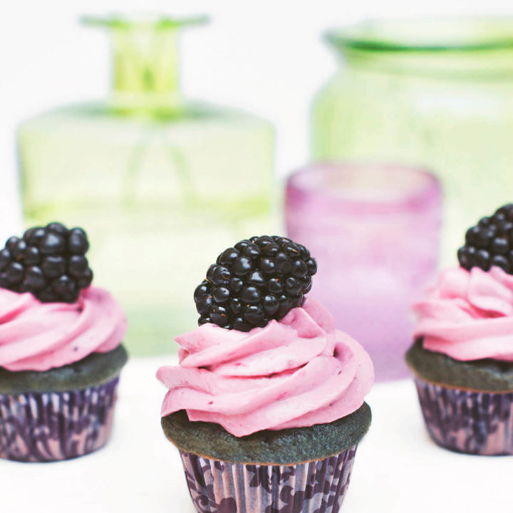 Closeup of mini blackberry cupcakes with green glass bottles behind it