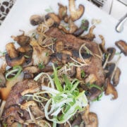 Overhead view of a serving plate with flank steak cut into slices and served with exotic mushrooms and garnished with chive slivers