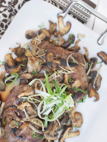 Overhead view of a serving plate with flank steak cut into slices and served with exotic mushrooms and garnished with chive slivers