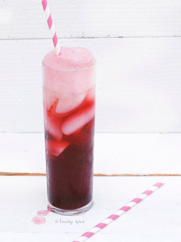 A tall glass of foamy pomegranate shirley temple with striped straw on a white background