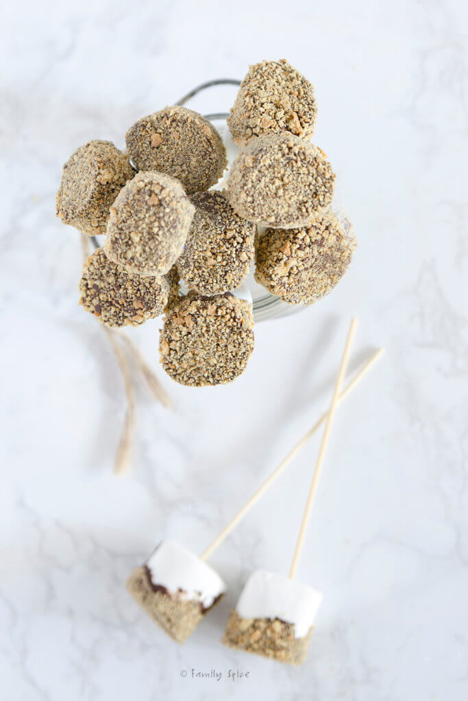 Top view of a bunch of marshmallows on a stick dipped in chocolate and coated with graham cracker crumbs in a glass jar