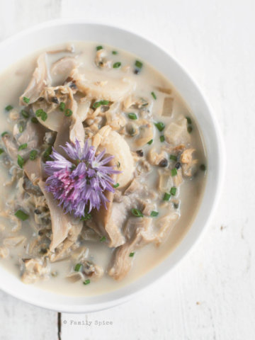 Overhead shot of a white bowl filled with asian clam chowder topped with a chive flower