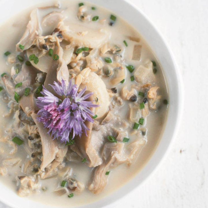 Overhead shot of a white bowl filled with asian clam chowder topped with a chive flower