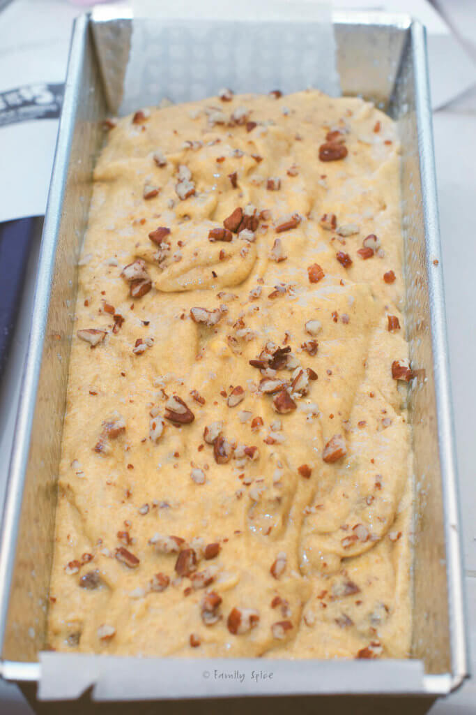 Mango bread batter topped with nuts in a metal loaf pan