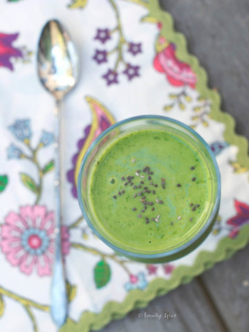 Top view of a bright green smoothie topped with chia seeds in a tall stemmed glass with floral napkin