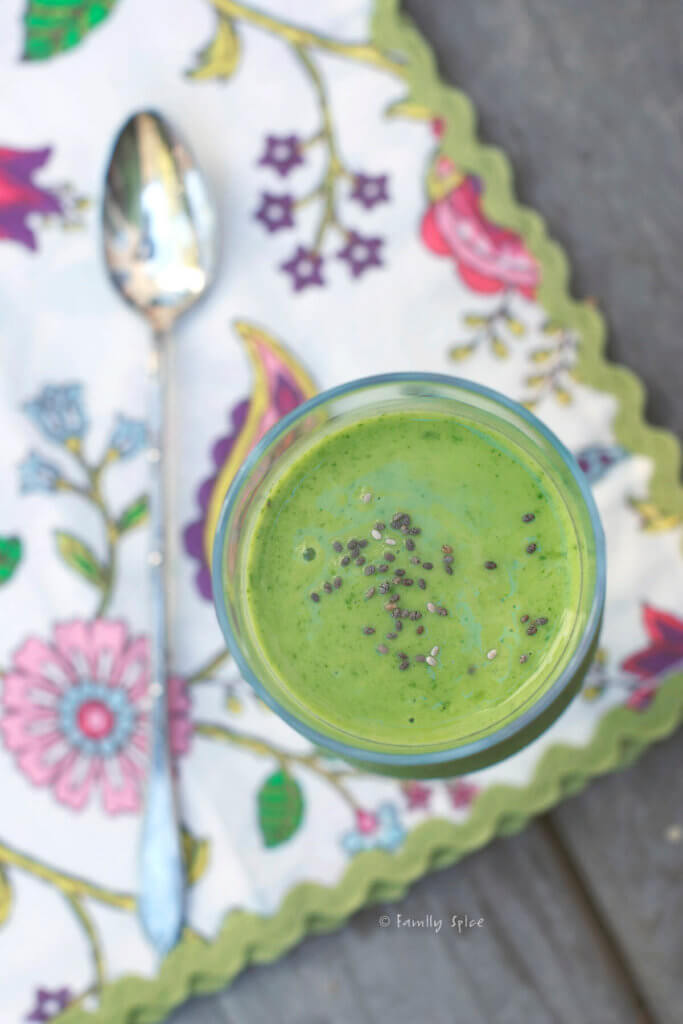 Top view of a bright green smoothie topped with chia seeds in a tall stemmed glass with floral napkin