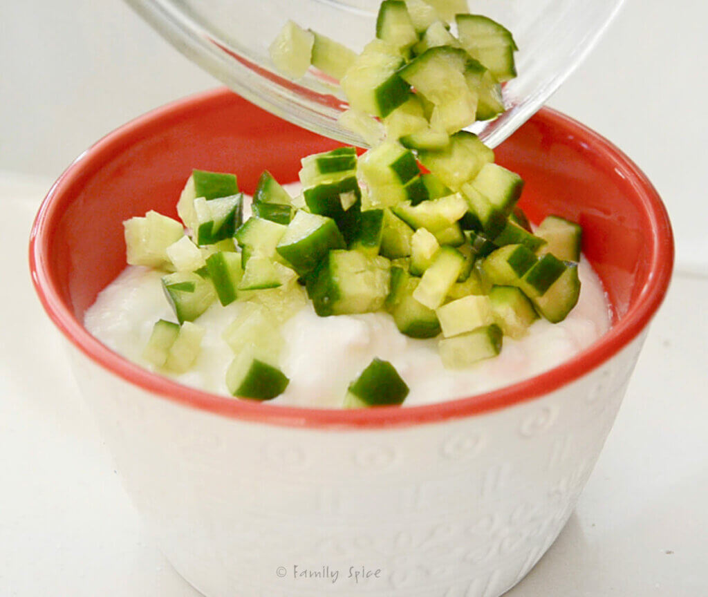 Adding diced cucumbers to a bowl with yogurt in it