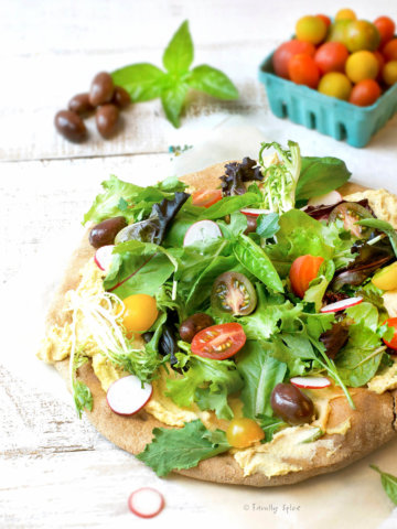 Whole wheat pizza crust topped with hummus, salad greens, tomatoes and olives