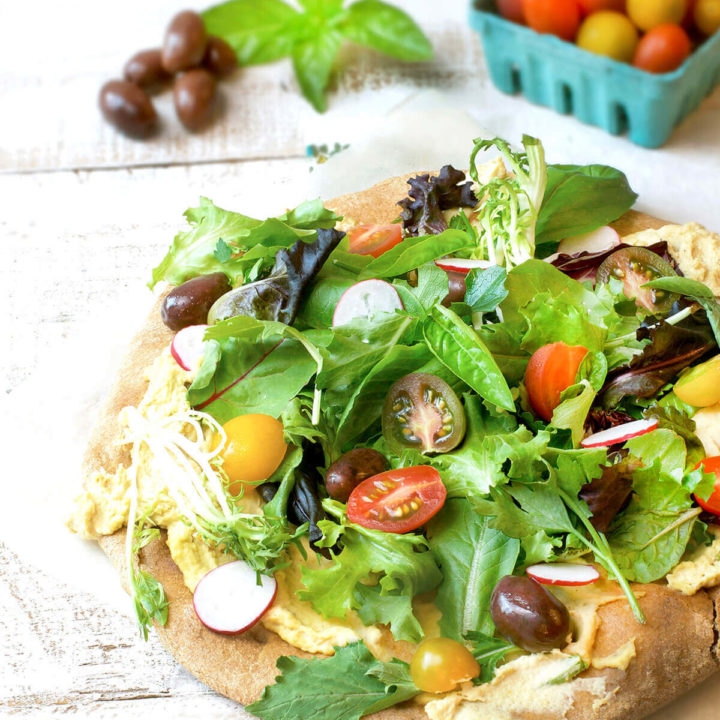 Whole wheat pizza crust topped with hummus, salad greens, tomatoes and olives