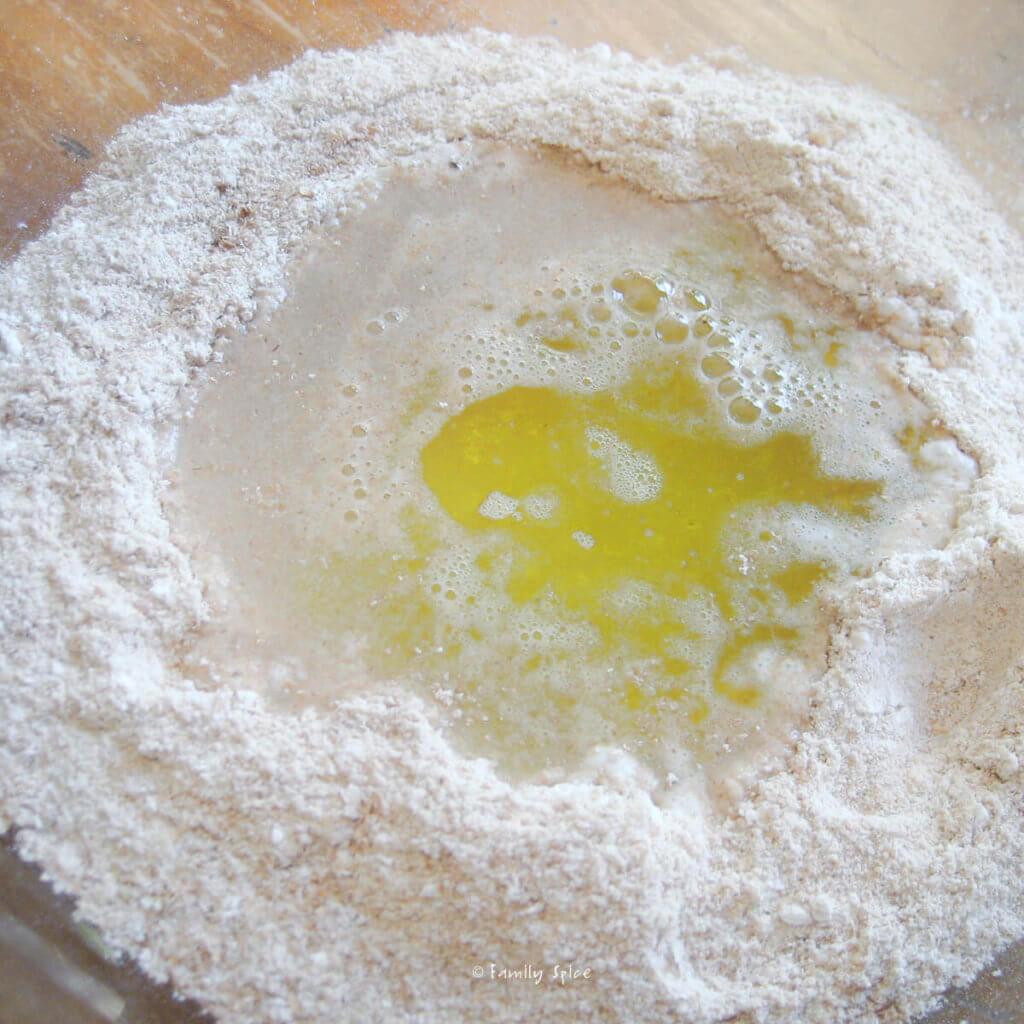A glass bowl with whole wheat flour, yeast, water and olive oil to make whole wheat pizza
