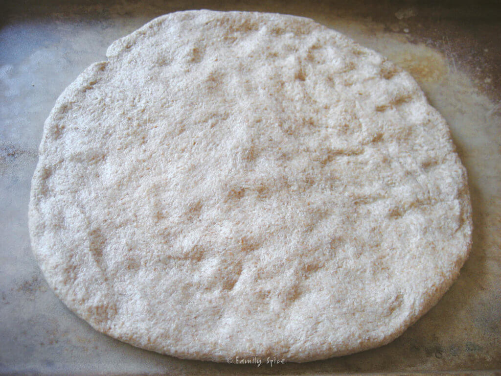 Whole wheat pizza dough pressed into a circle on a baking sheet