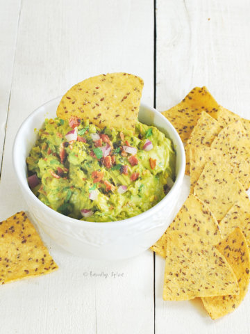 A bowl of smoky guacamole with bacon with chips next to it