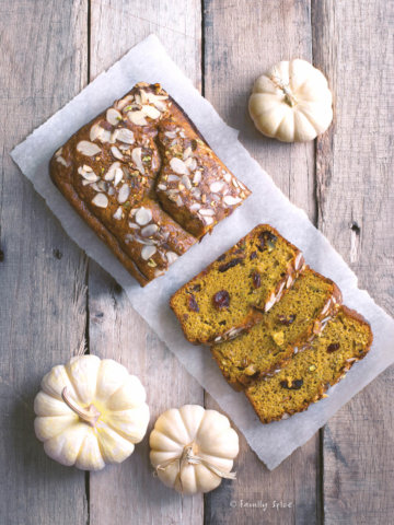 A loaf of gluten pumpkin bread on a wood table with sliced pieces and small white pumpkins around it