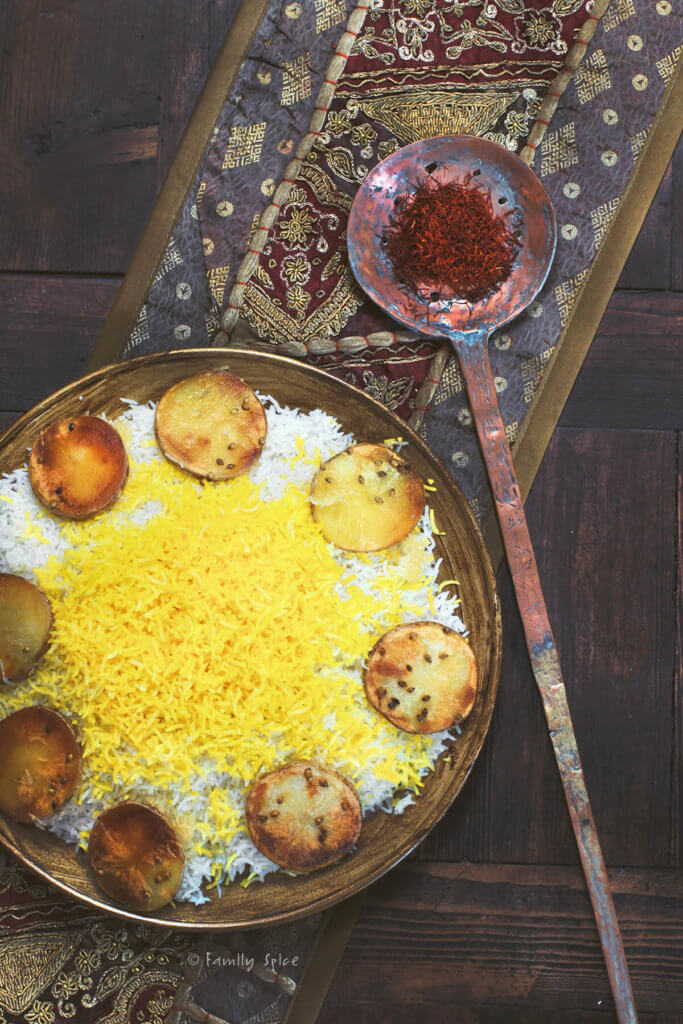 A round gold platter of Persian rice topped with saffron rice with rounds of potato tadig on a dark surface