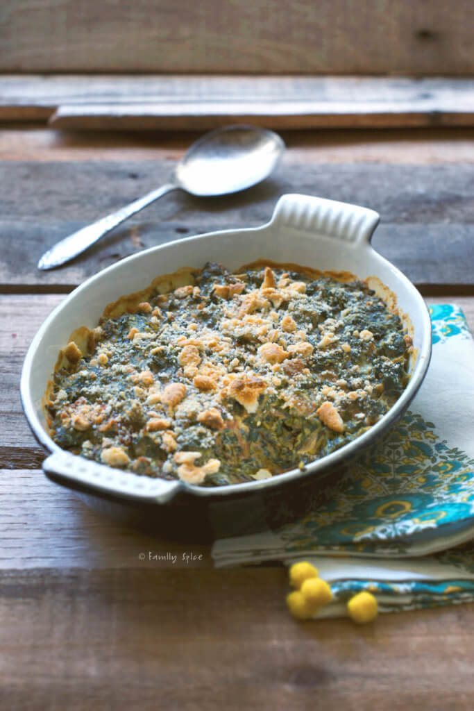 Side view of baked creamed spinach topped with cracker crumbles on a rustic background