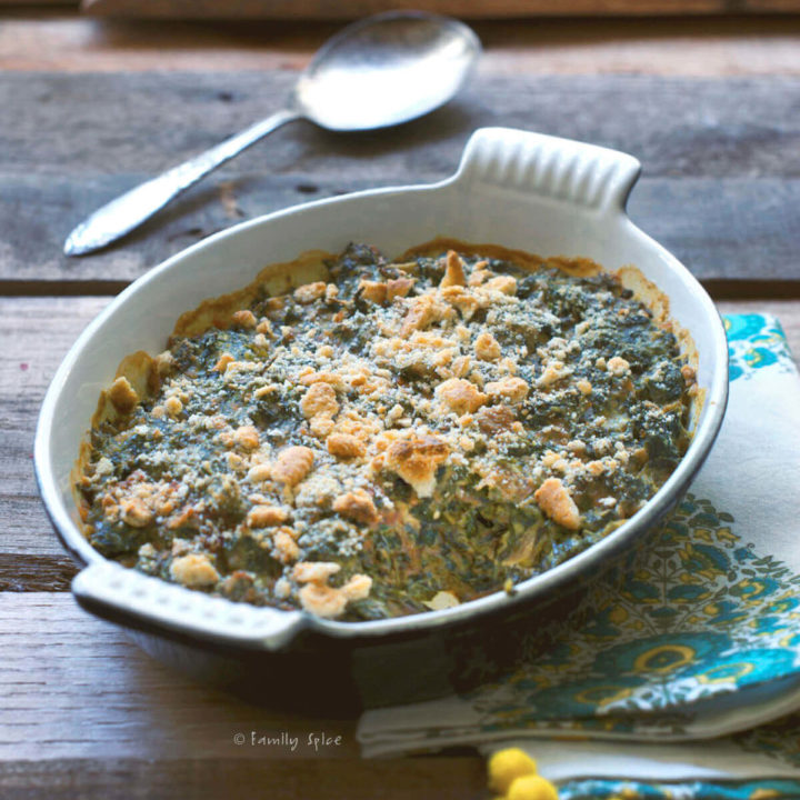 Side view of baked creamed spinach topped with cracker crumbles on a rustic background