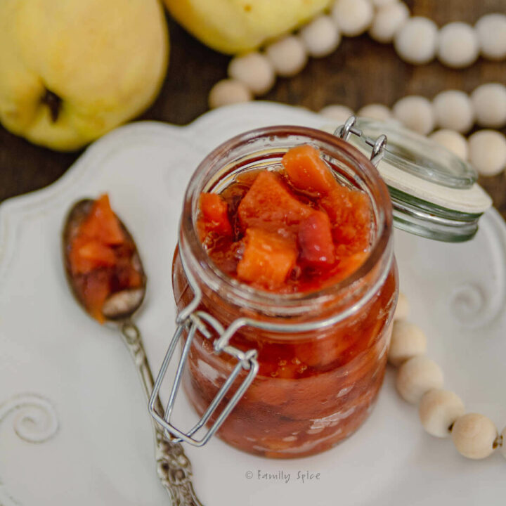 Closeup of a mason jar with red quince jam on a white plate