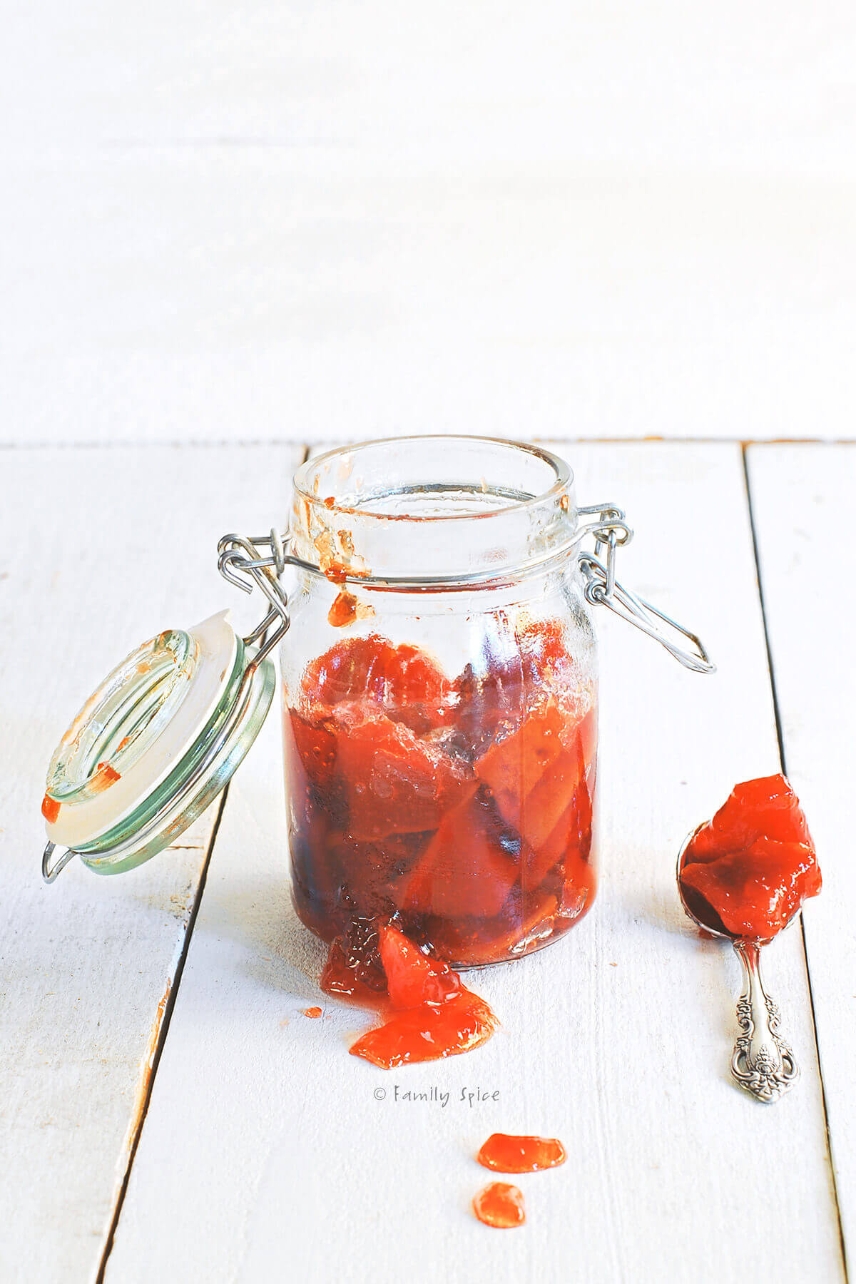 An old mason jar with red quince jam chunks inside with a spoon of jam next to it