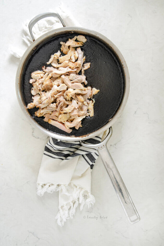A stainless pan with chicken slices added to the pomegranate walnut sauce for fesenjoon in it