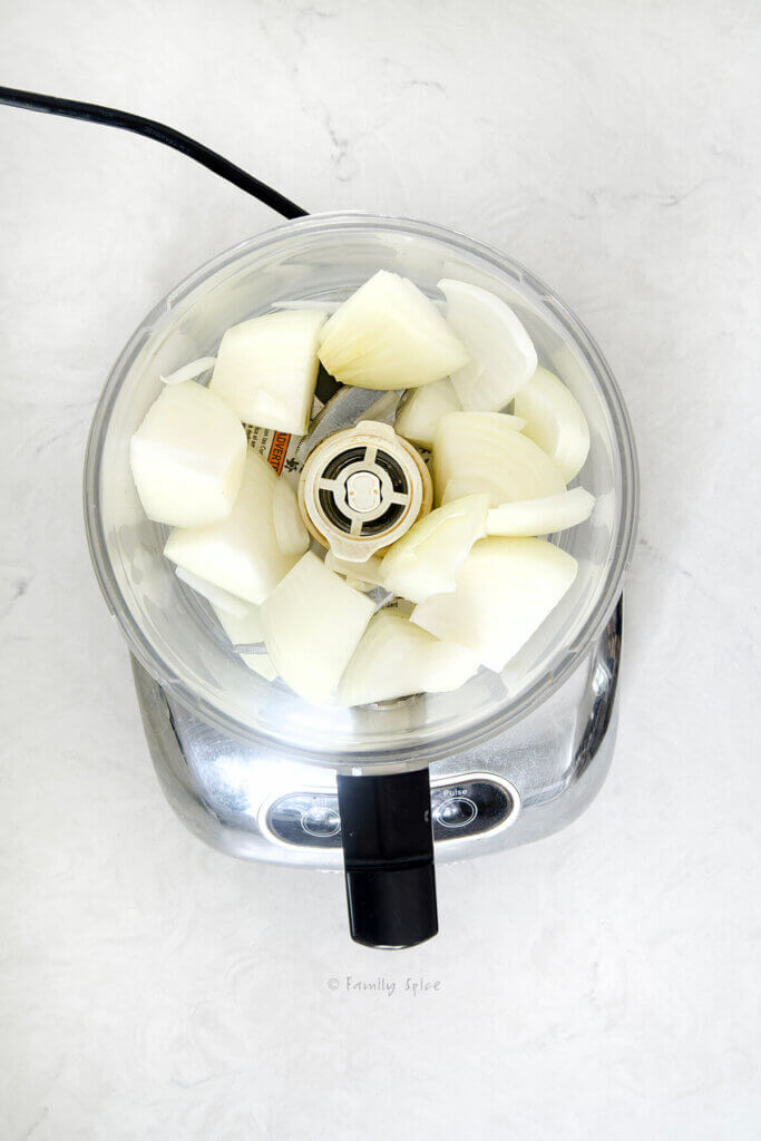 Top view of a food processor bowl with wedges of cut onions in it