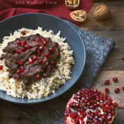 A bowl of Persian Pomegranate and Walnut Stew (Fesenjoon) over brown rice next to half a pomegranate