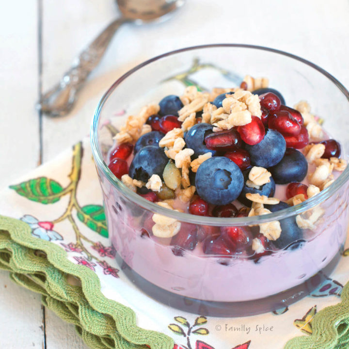 Closeup of a glass bowls with pomegranate parfait topped with blueberries, pomegranate arils, walnuts and granola
