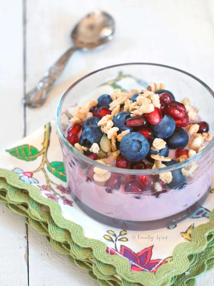 Closeup of a glass bowls with pomegranate parfait topped with blueberries, pomegranate arils, walnuts and granola