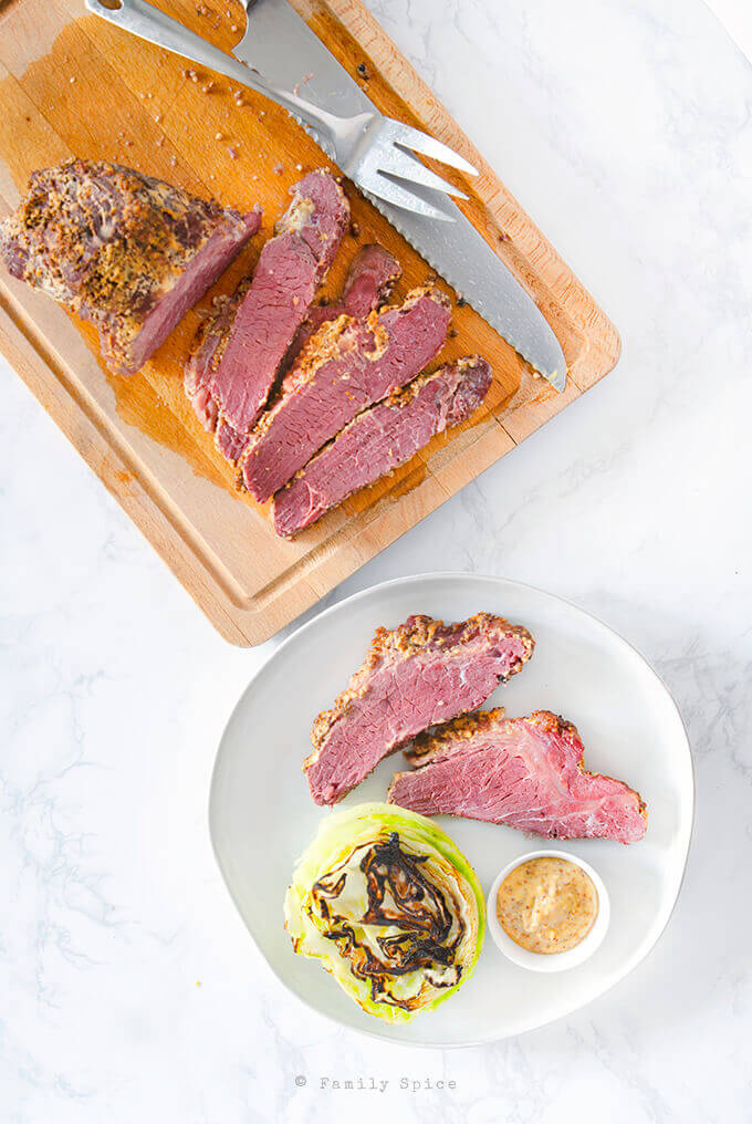 Baked corned beef sliced on a cutting board with a plate by FamilySpice.com
