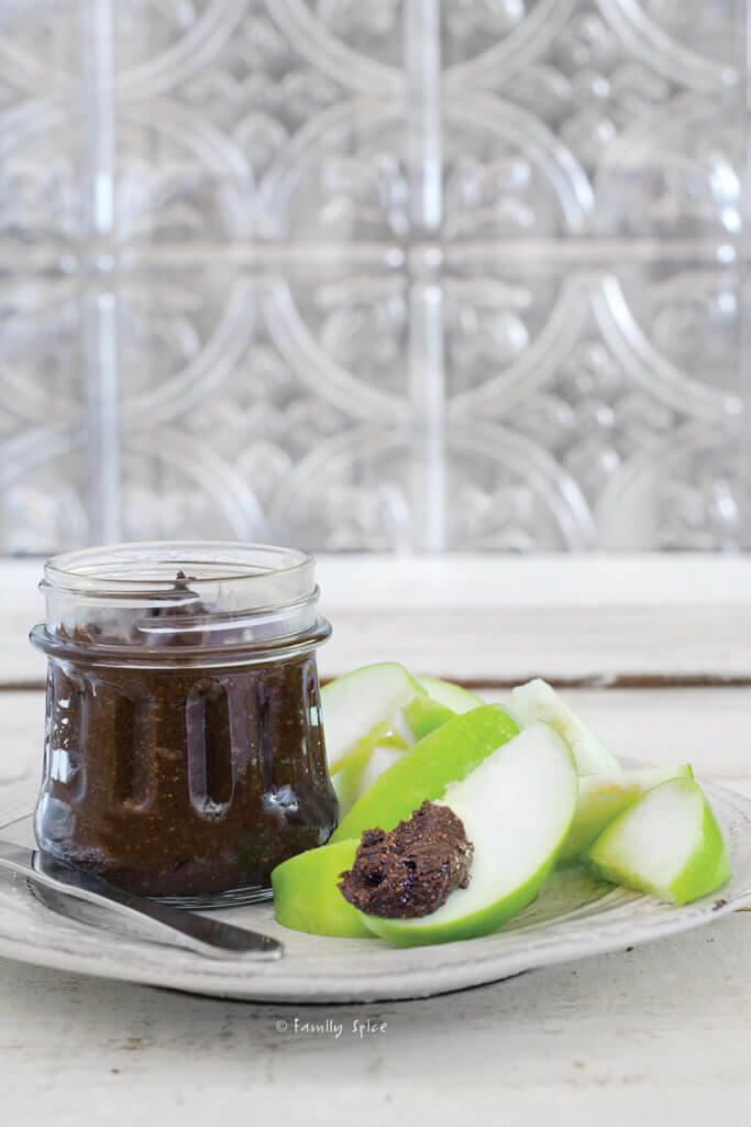 Side view of a jar of carob butter with slices of green apples
