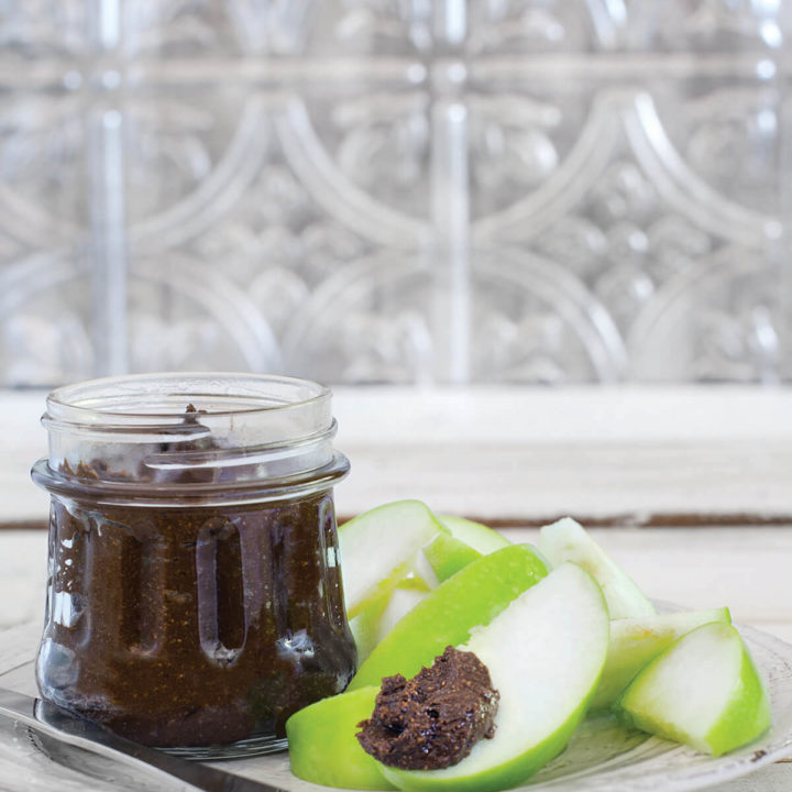 Side view of a jar of carob butter with slices of green apples