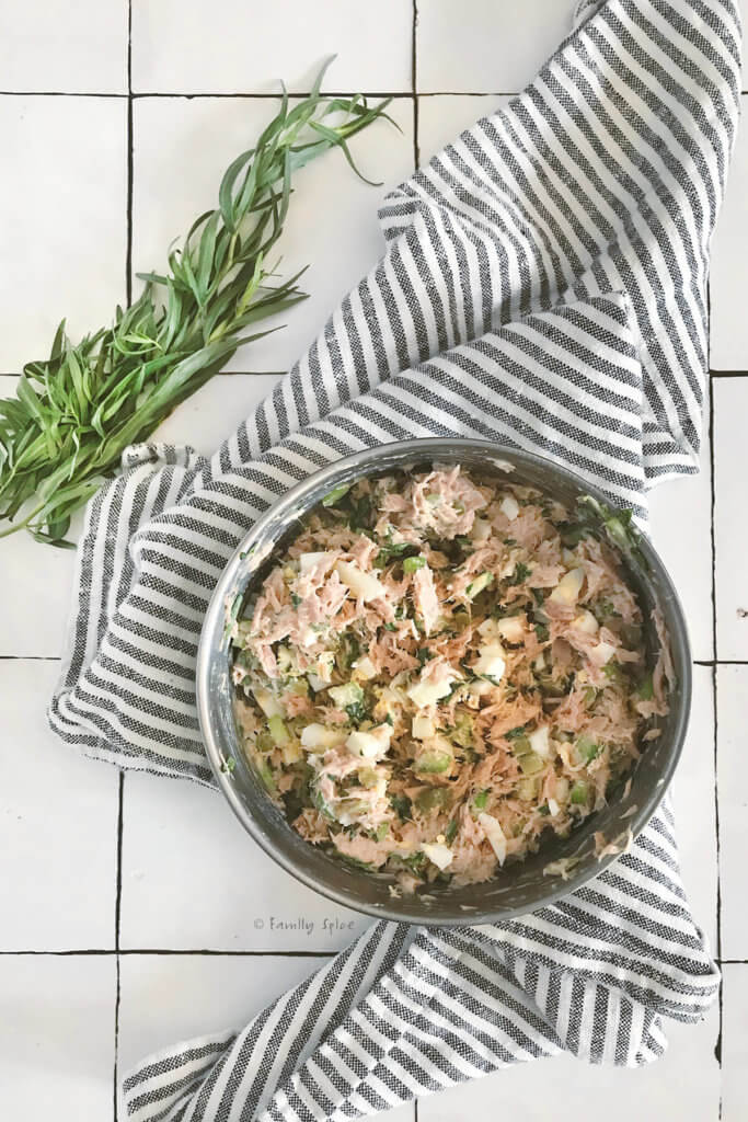 Tuna egg salad mixed in a stainless bowl with tarragon next to it