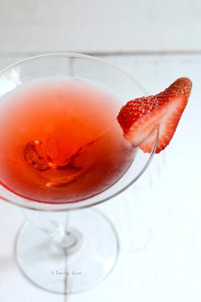 Top view of a crooked martini glass with strawberry martini in it and a slice of strawberry on the rim
