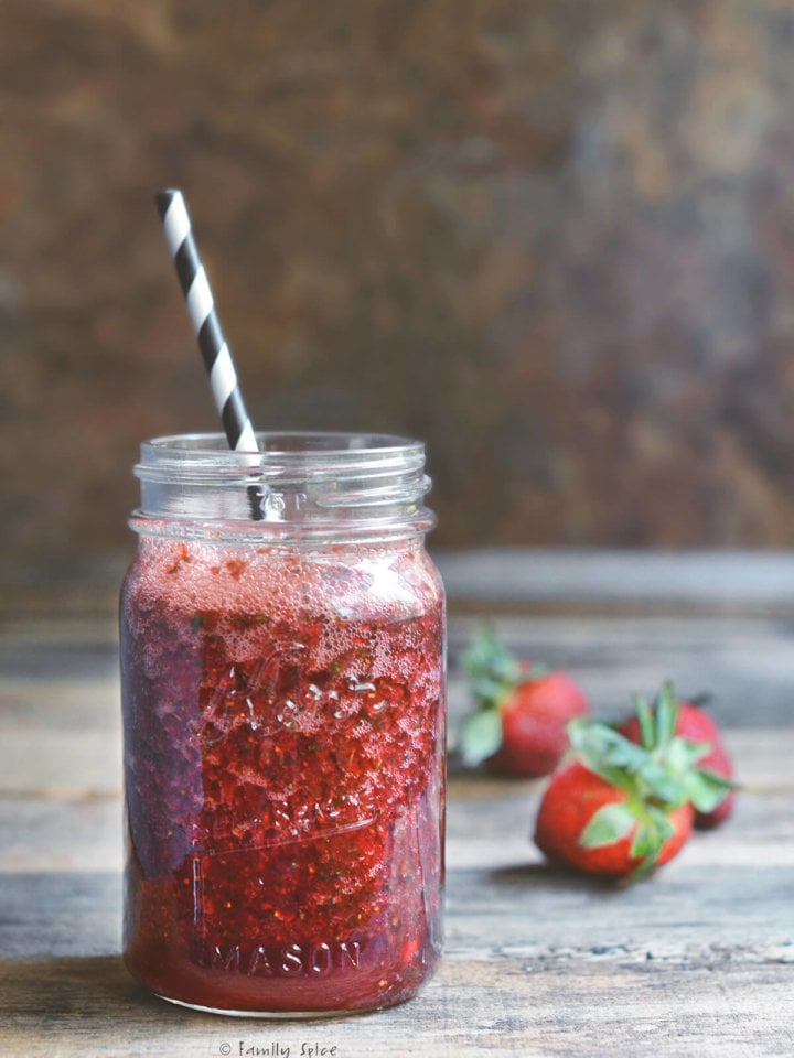 Side view of a mason jar glass filled with strawberry drink with a black and white striped straw
