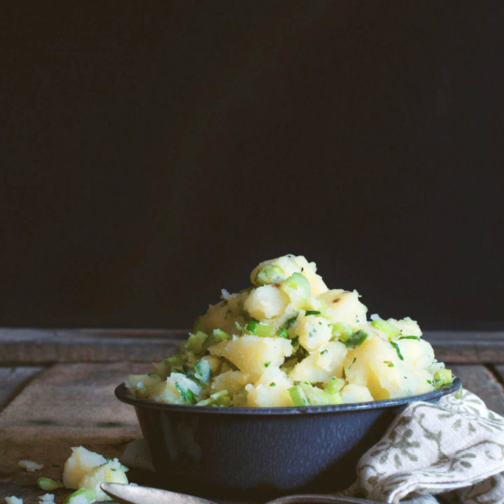 A grey bowl with mayo free potato free potato salad with green onions and celery
