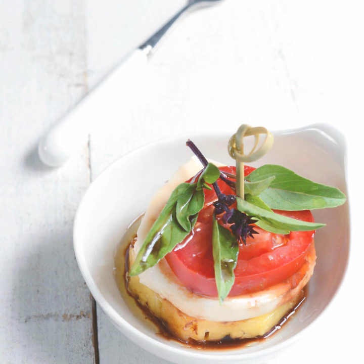 A single portion of pineapple caprese (pineapple slice, mozzarella, tomato, and basil) drizzled with olive oil and balsamic vinegar