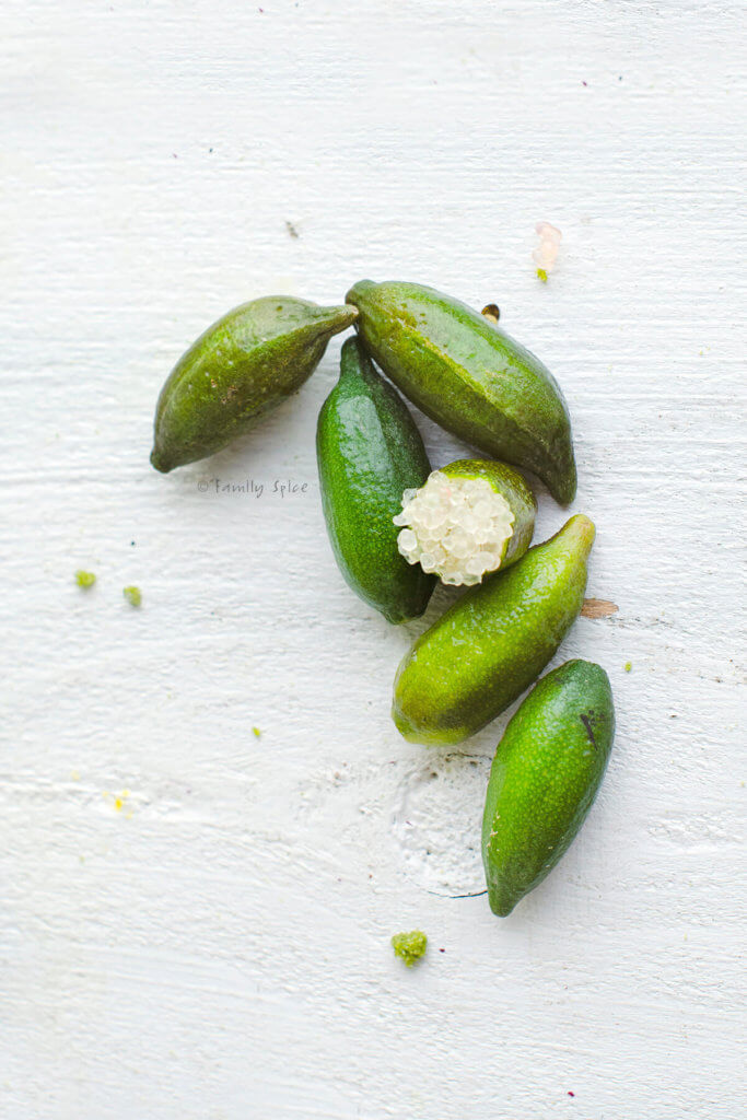 Several finger limes on a white wood background with one cut open