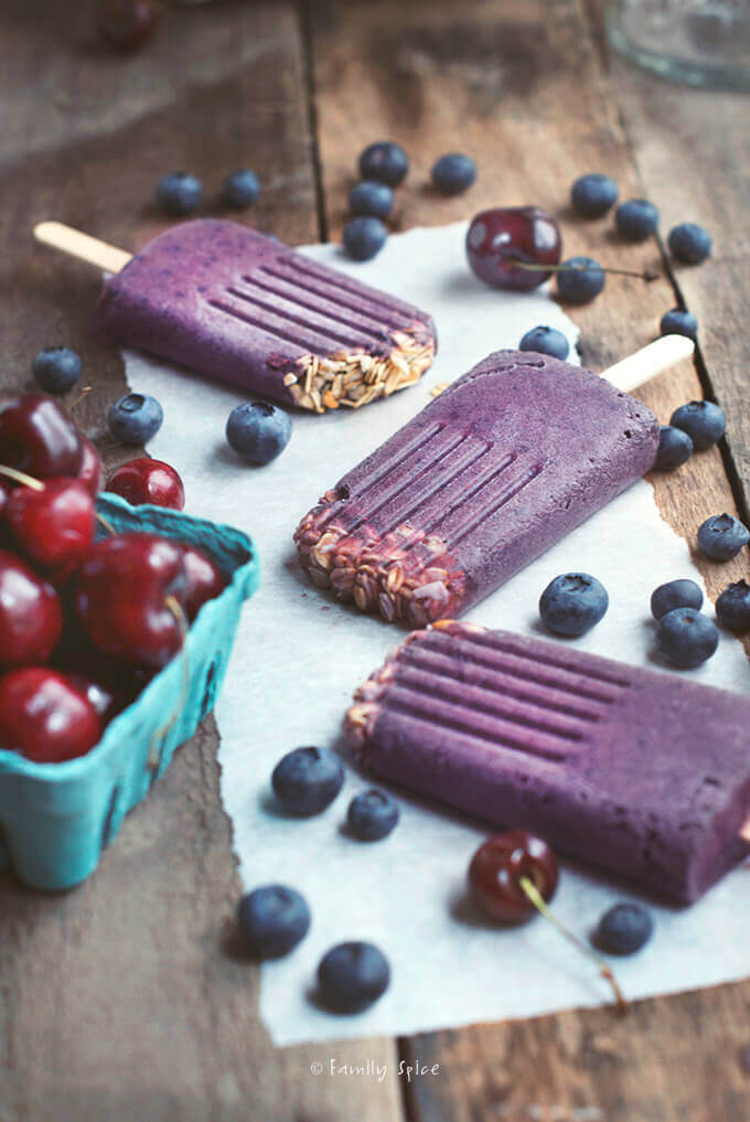 Three purple smoothie popsicles made with blueberries, cherries and granola by FamilySpice.com