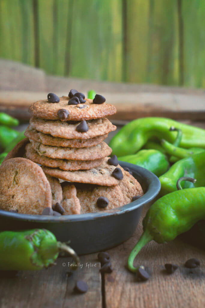 A stack of chocolate chip cookies made with and surrounded by green Hatch chiles