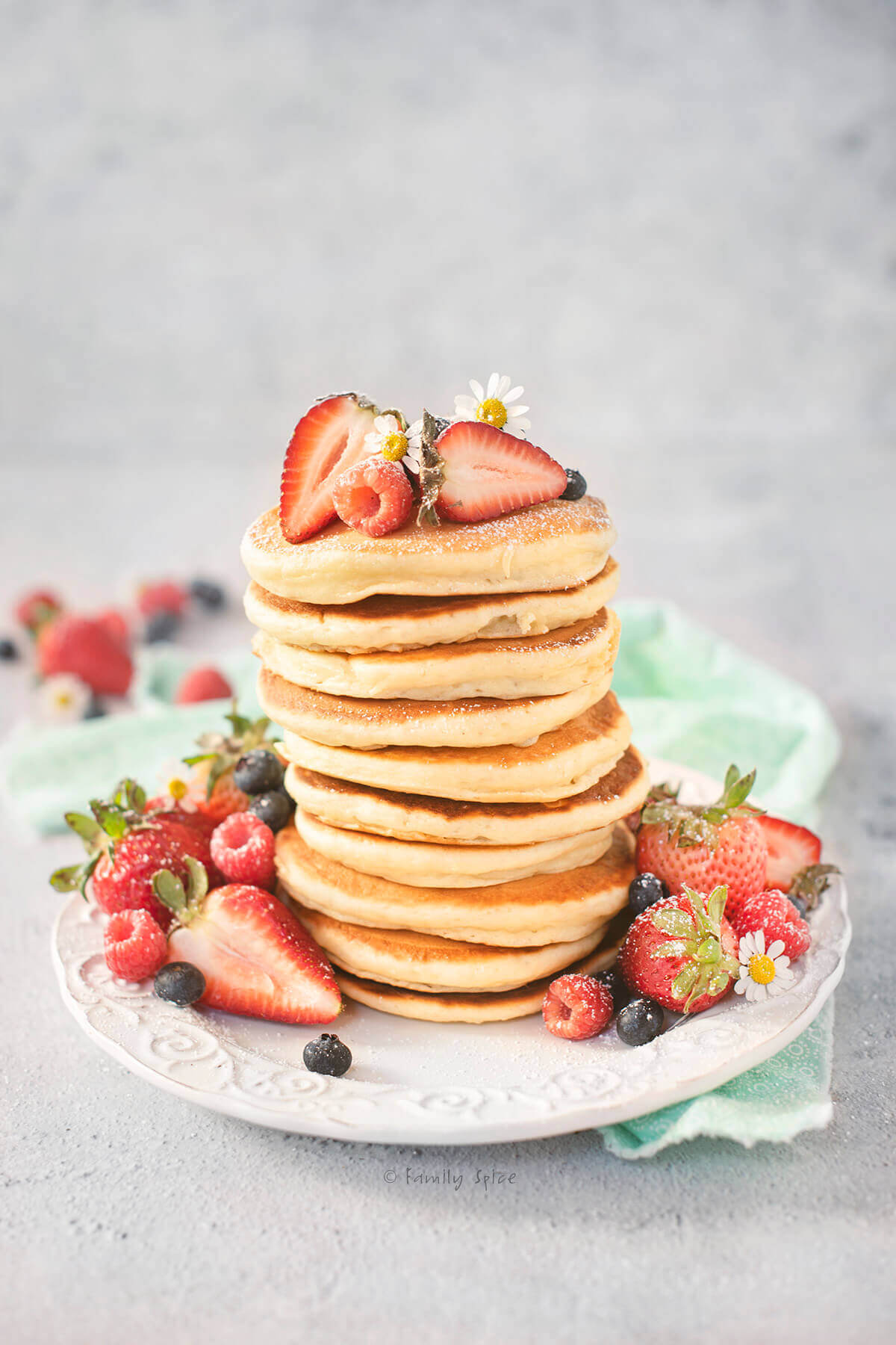Side view of a stack of yogurt pancakes topped and surrounded with fresh berries