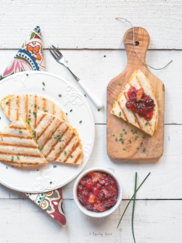 A plate of turkey quesadillas cut up with one section on a cutting board with a bowl of cranberry sauce