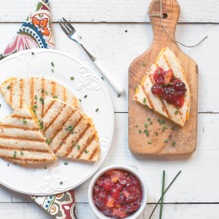A plate of turkey quesadillas cut up with one section on a cutting board with a bowl of cranberry sauce