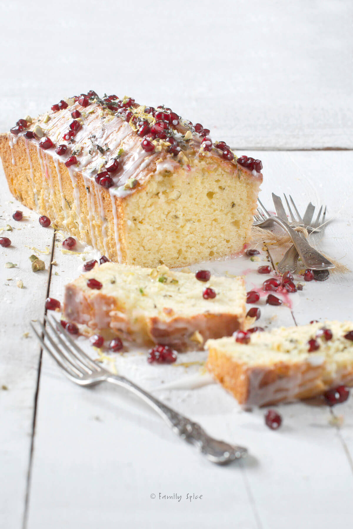 An olive oil lemon cake baked in a loaf pan and garnished with pistachios and pomegranate arils