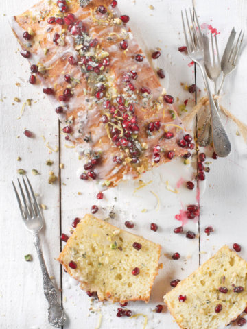 Top view of a olive oil lemon cake baked in a loaf pan and garnished with pistachios and pomegranate arils with slices next to it