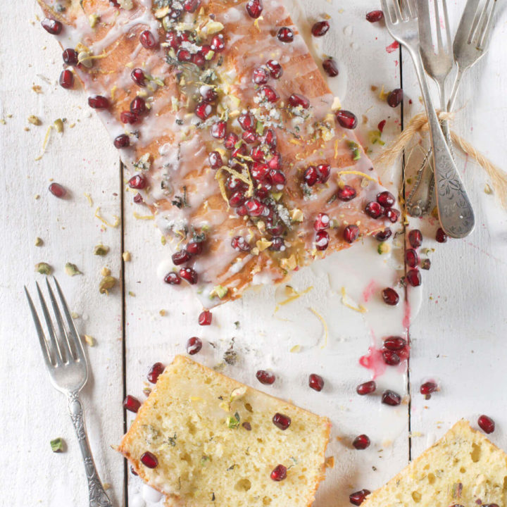 Top view of a olive oil lemon cake baked in a loaf pan and garnished with pistachios and pomegranate arils with slices next to it