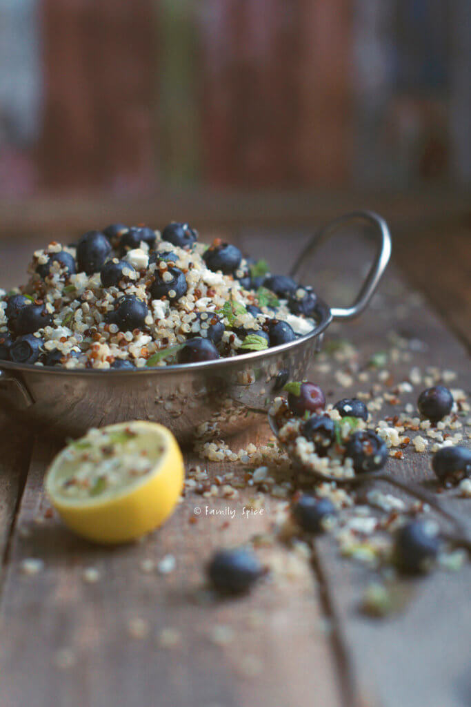 Closeup of a metal bowl with handles with blueberry quinoa salad with feta and lime half next to it