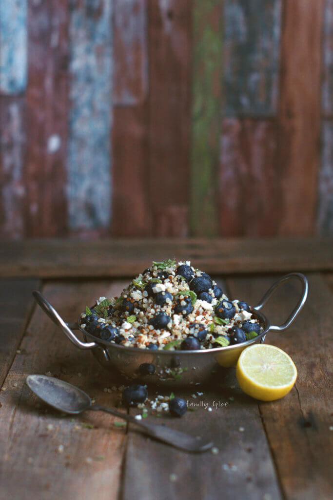 A metal bowl with handles with blueberry quinoa salad with feta and lime half next to it