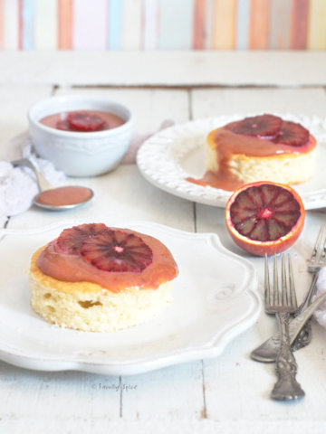 Side view of two plates with small cakes topped with blood orange curd with a bowl of blood orange curd next to it