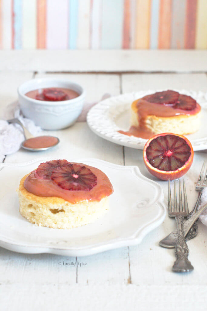 Side view of two plates with small cakes topped with blood orange curd with a bowl of blood orange curd next to it