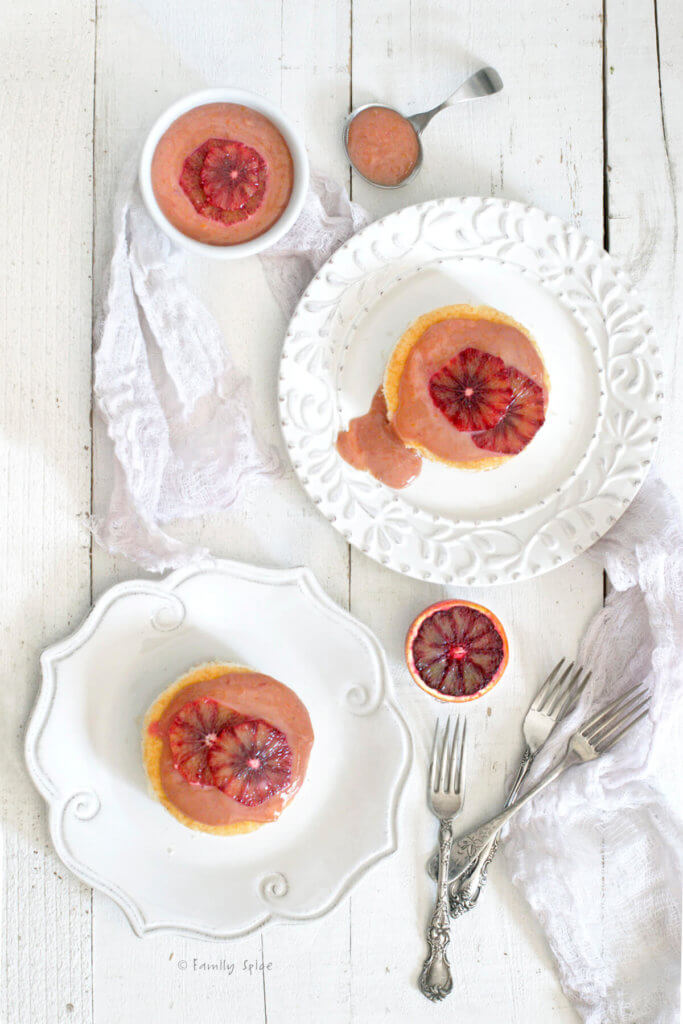Top view of two plates with small cakes topped with blood orange curd with a bowl of blood orange curd next to it